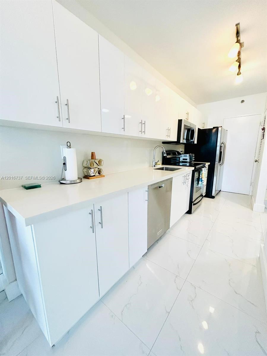 A modern kitchen features white cabinets, stainless steel appliances, and white marble-patterned tile flooring — 100 Lincoln Rd # 1526, Miami Beach FL 33139, MIAMI BEACH, FL