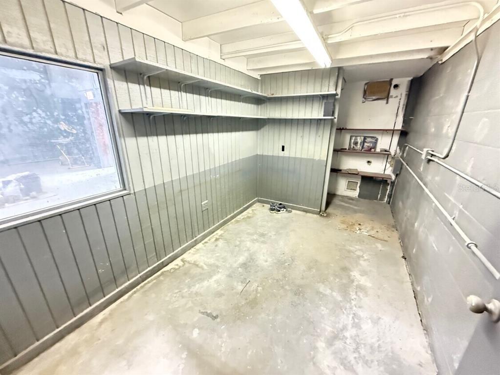 A utility room with gray paneled walls, concrete flooring, and built-in wooden shelving — 14041 NW 20TH AVENUE, OPA LOCKA, FL