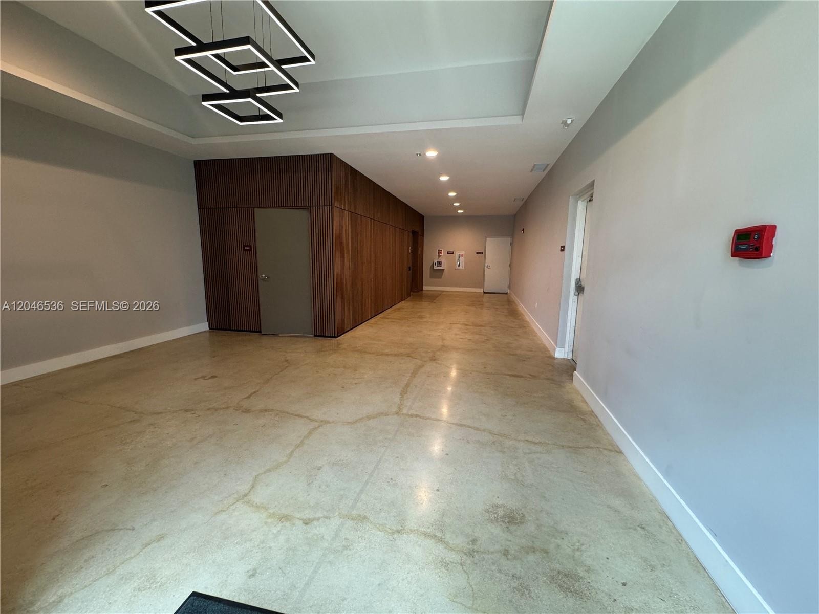 A modern hallway features a concrete floor, wood-slatted wall paneling, and geometric ceiling lights — 1938 Jackson St # 503, Hollywood FL 33020, HOLLYWOOD, FL