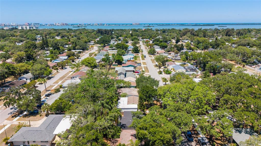 An aerial view shows a residential neighborhood with houses, lush trees, and a distant coastline — 1275 PALM STREET, CLEARWATER, FL