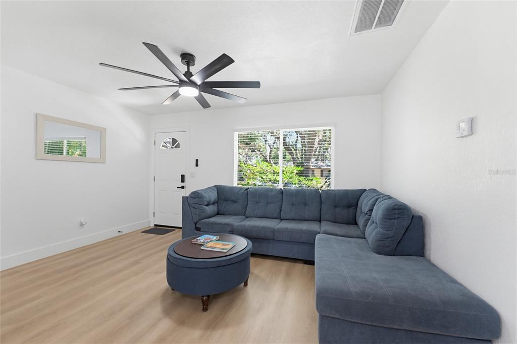 A living room features light wood-look flooring, a blue sectional sofa, and a ceiling fan — 1275 PALM STREET, CLEARWATER, FL