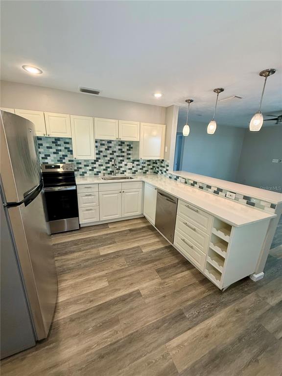 A kitchen with white cabinets, stainless steel appliances, a tiled backsplash, and wood-look flooring — 2716 BLOSSOM DRIVE, SARASOTA, FL