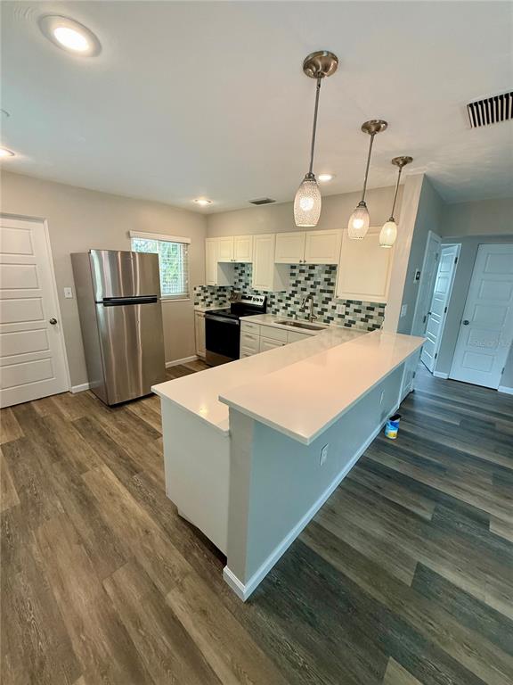 A kitchen features white cabinets, a stainless steel refrigerator, a quartz island, and wood-look flooring — 2716 BLOSSOM DRIVE, SARASOTA, FL
