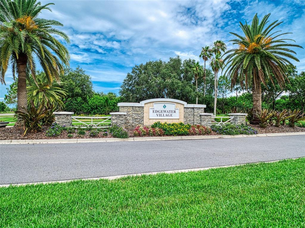 A stone monument sign for Edgewater Village sits behind a paved road and green lawn — 8310 WHISPERING WOODS COURT, BRADENTON, FL