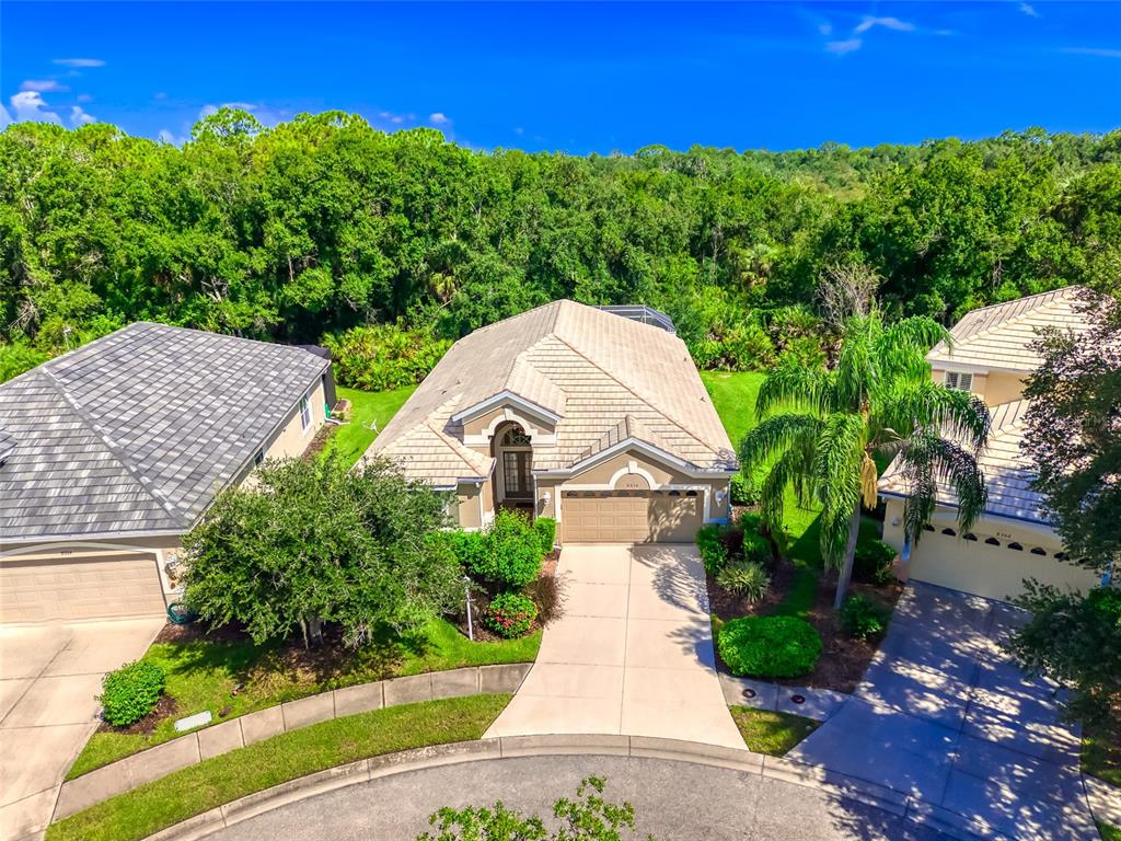 An aerial view shows a suburban house with a tan roof and driveway — 8310 WHISPERING WOODS COURT, BRADENTON, FL