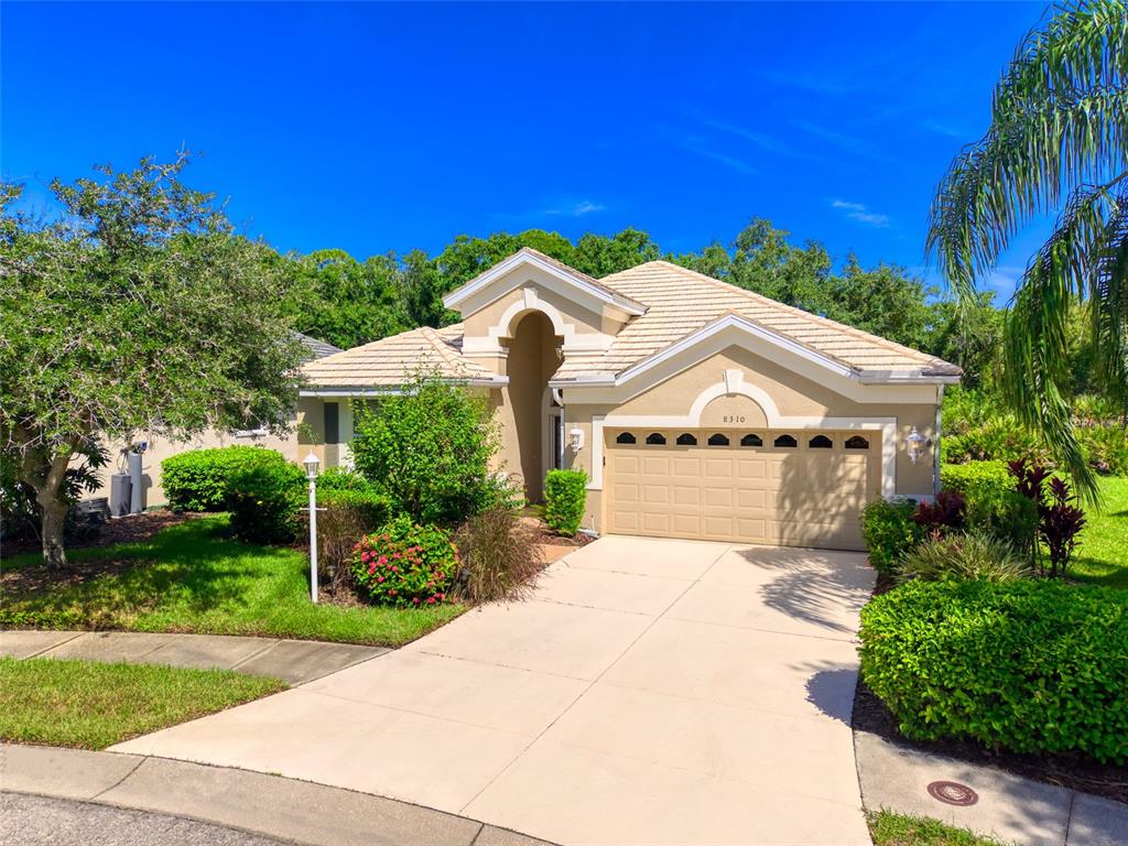 A single-story house with a tan stucco exterior, a tiled roof, and a two-car garage — 8310 WHISPERING WOODS COURT, BRADENTON, FL