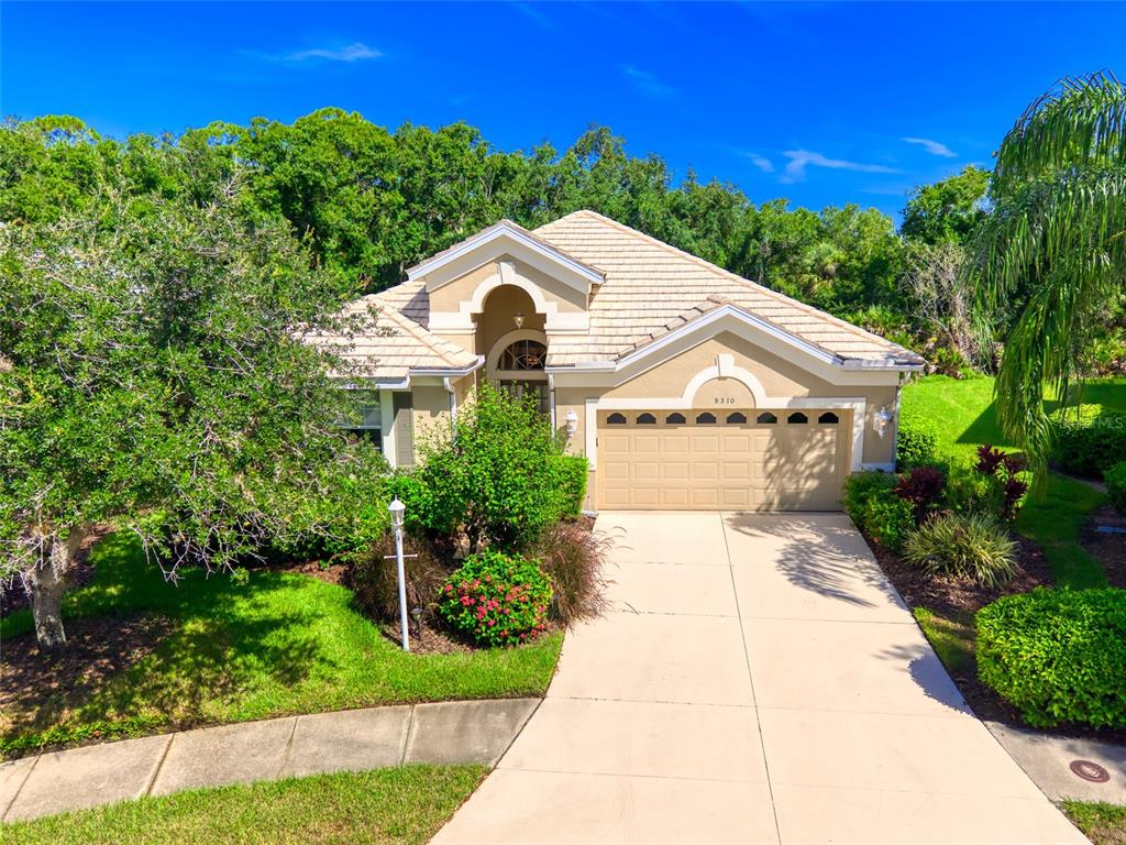 A single-story suburban house features a tan stucco exterior, a tiled roof, and a garage — 8310 WHISPERING WOODS COURT, BRADENTON, FL