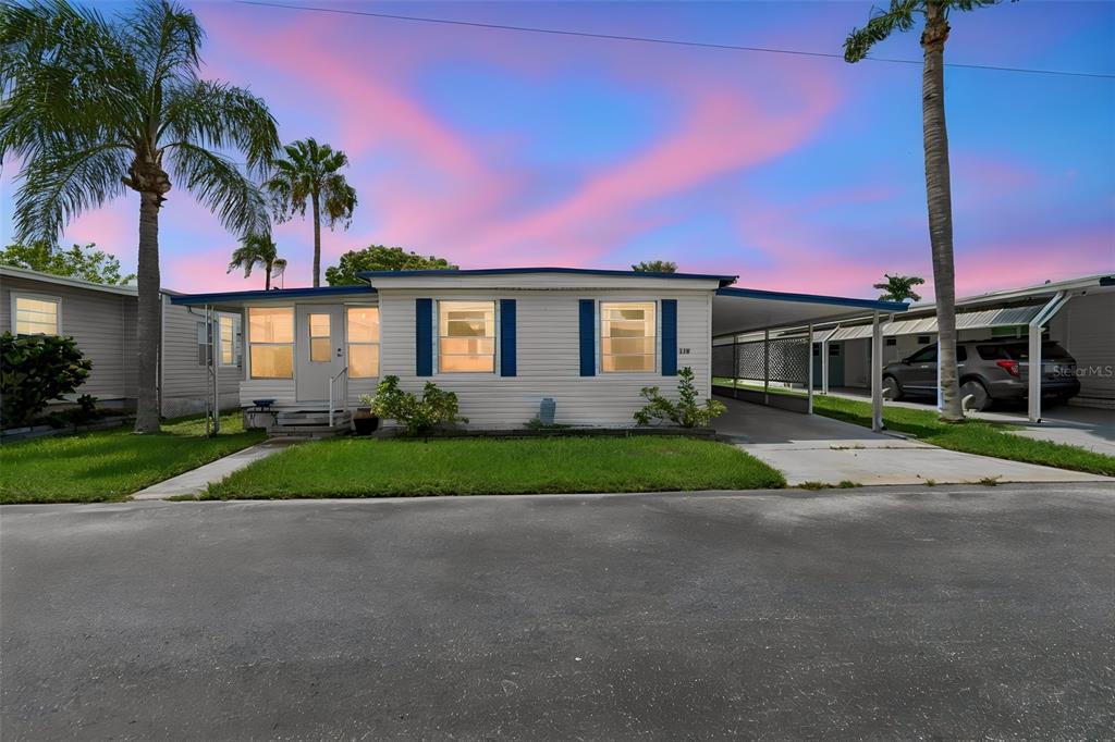 A single-story manufactured home with a carport and palm trees under a sunset sky — 18675 US HIGHWAY 19 N UNIT 116, CLEARWATER, FL