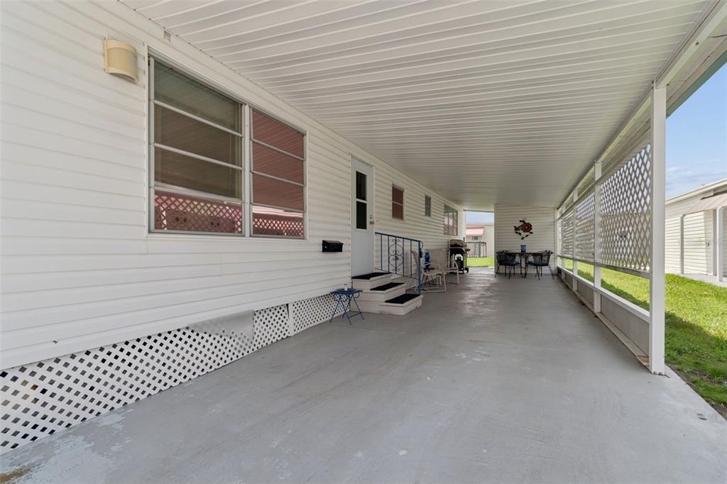 A long, covered concrete carport features white siding, lattice skirting, and a small entry staircase — 18675 US HIGHWAY 19 N UNIT 116, CLEARWATER, FL