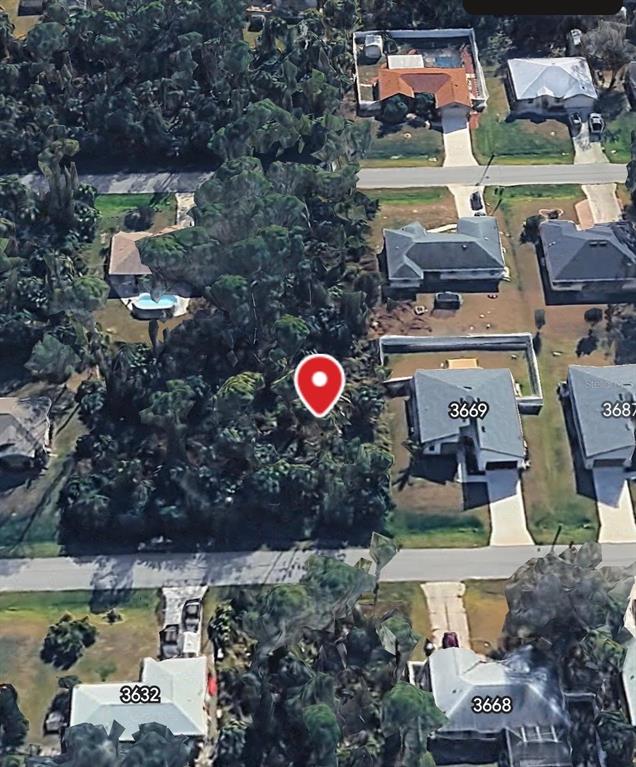 An aerial view shows a vacant, tree-covered lot situated between several residential houses — ZAMBRANA AVENUE, NORTH PORT, FL