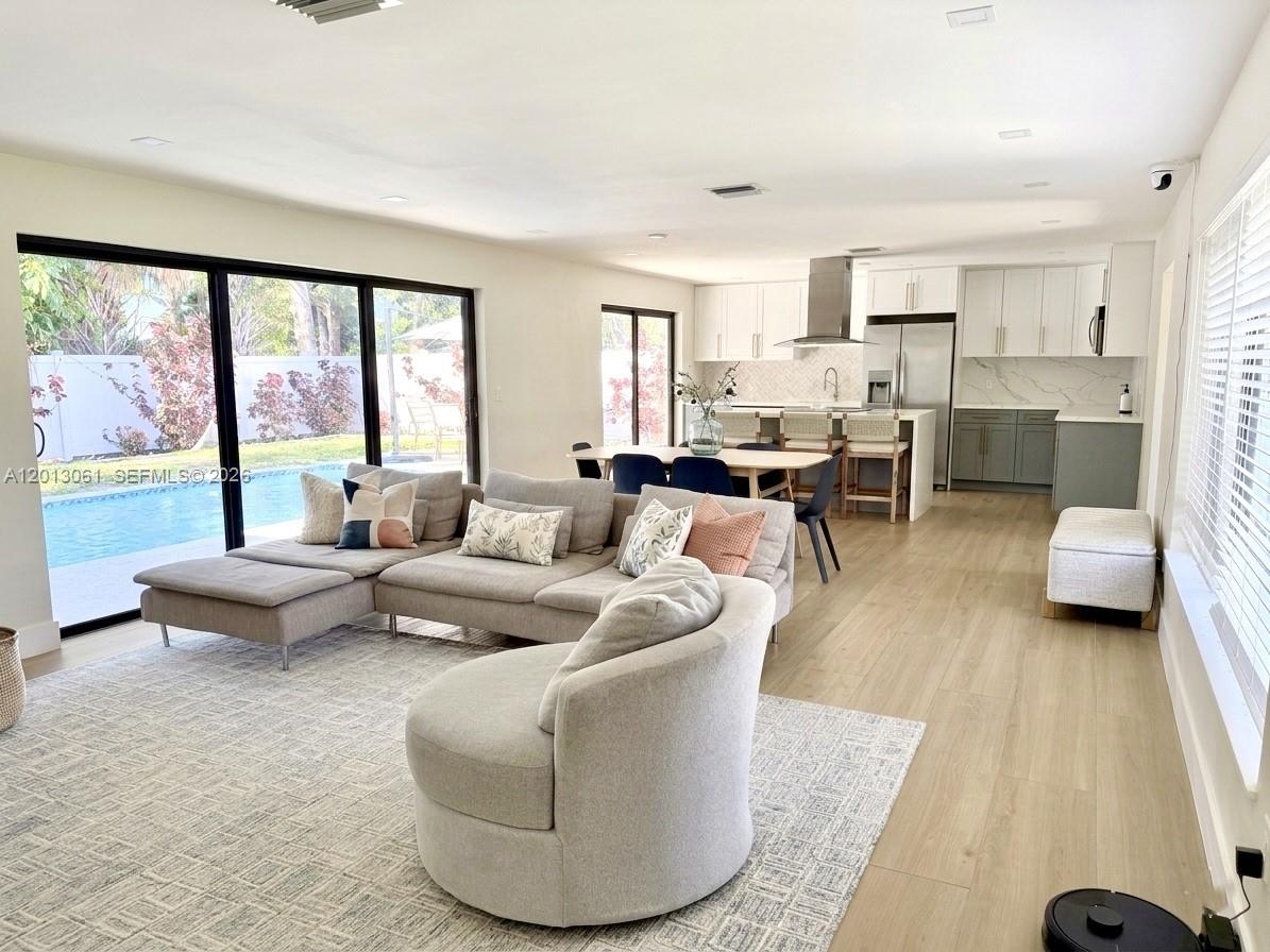 An open-concept living room and kitchen feature light wood flooring, a sectional sofa, and pool views — 151 SE 6th Ct, Pompano Beach FL 33060, POMPANO BEACH, FL