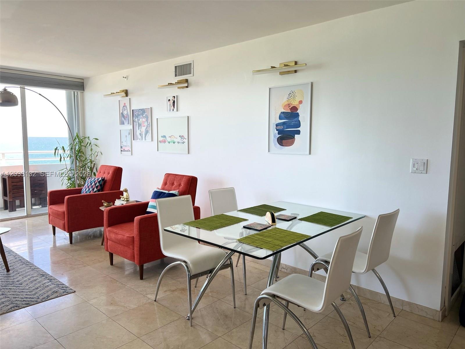 A dining area with a glass table and white chairs sits beside two orange armchairs — 8911 Collins Ave # 605, Surfside FL 33154, SURFSIDE, FL