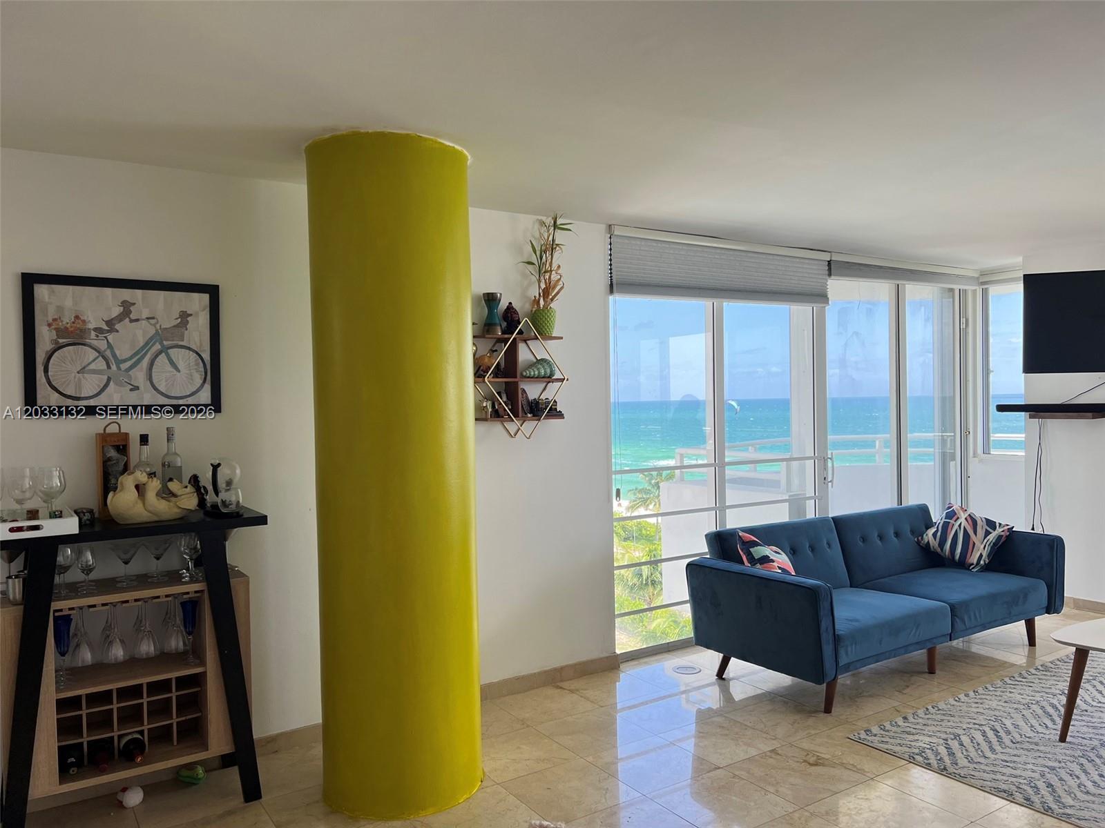 A living room features a bright yellow structural column, a blue sofa, and ocean views — 8911 Collins Ave # 605, Surfside FL 33154, SURFSIDE, FL