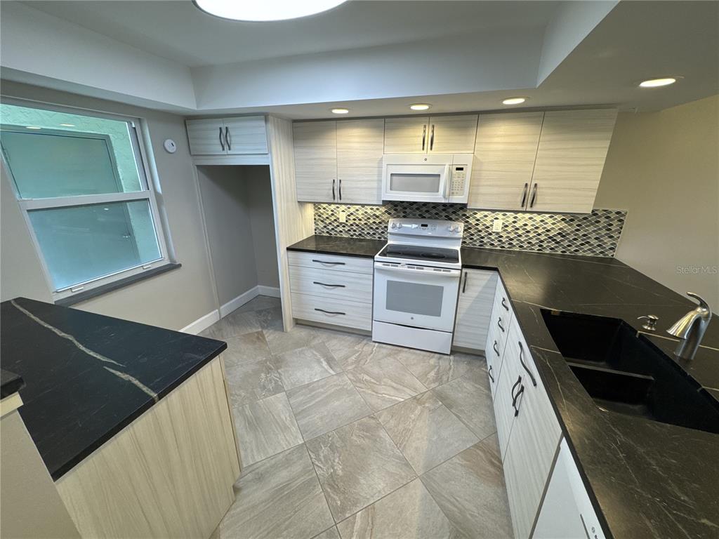 A kitchen features light wood cabinets, black countertops, a white stove, and tiled flooring — 3600 BAL HARBOR BOULEVARD UNIT 1G, PUNTA GORDA, FL