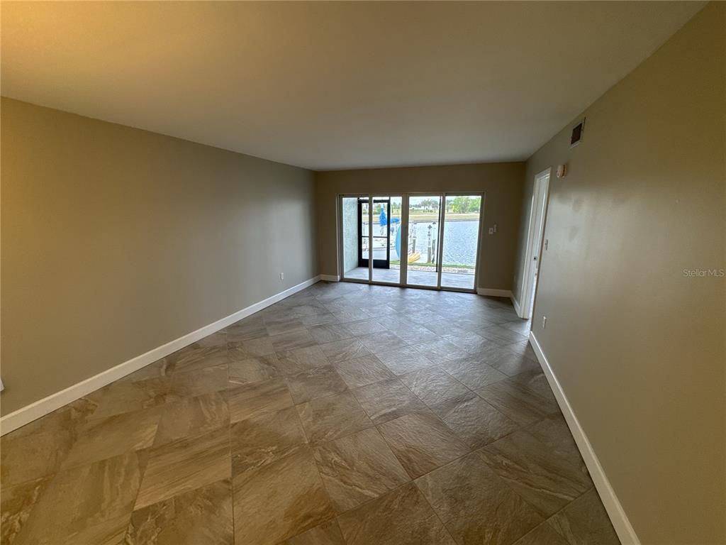 An empty room with tan walls, tile flooring, and sliding glass doors overlooking a canal — 3600 BAL HARBOR BOULEVARD UNIT 1G, PUNTA GORDA, FL