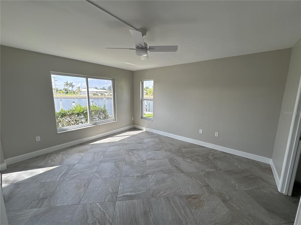 An empty room features gray walls, large tile flooring, a ceiling fan, and waterfront views — 3600 BAL HARBOR BOULEVARD UNIT 1G, PUNTA GORDA, FL