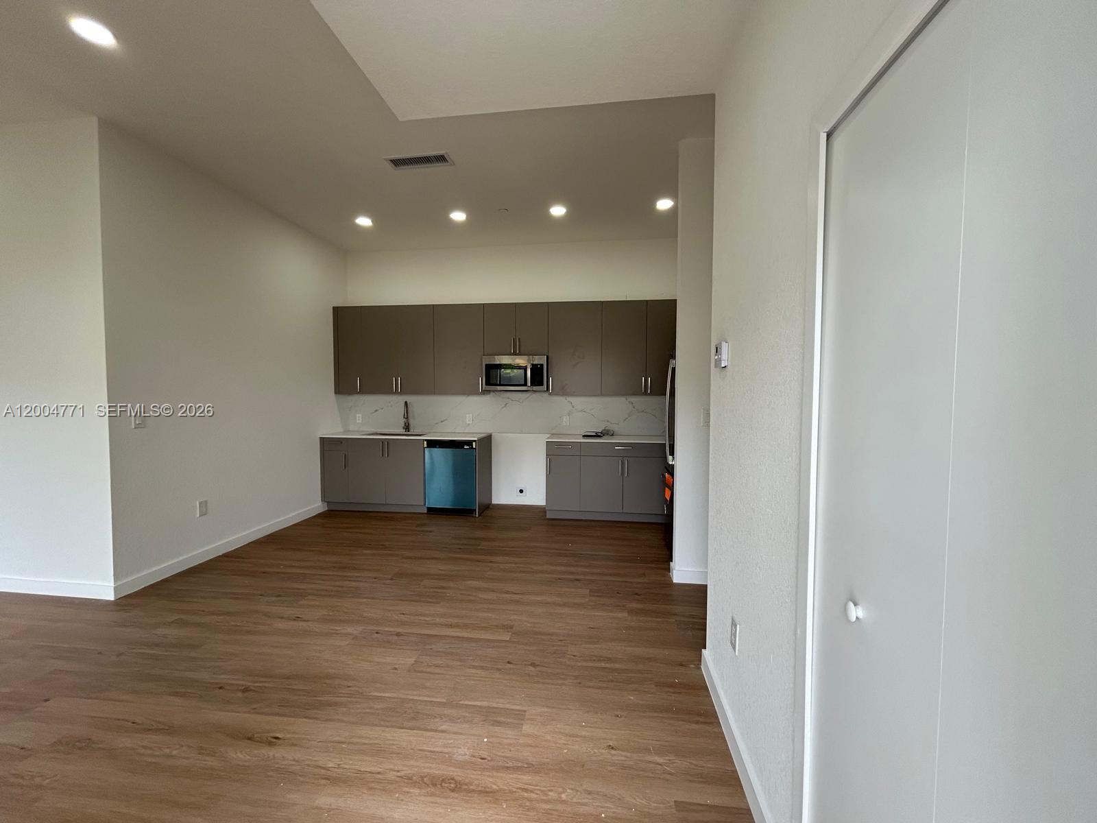 A modern kitchen features grey flat-panel cabinets, stainless steel appliances, and light wood flooring — 19428 SW 125th AVE # 0, Miami FL 33177, MIAMI, FL