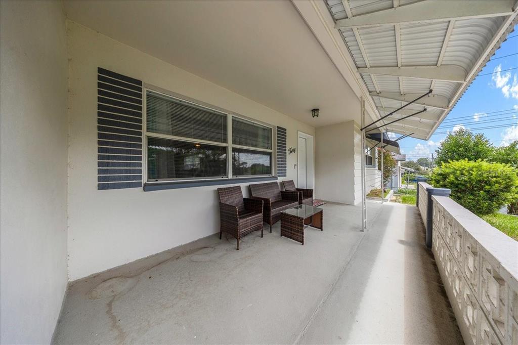 A covered concrete porch features wicker patio furniture and a decorative block wall railing — 30 N LINCOLN AVENUE, BEVERLY HILLS, FL