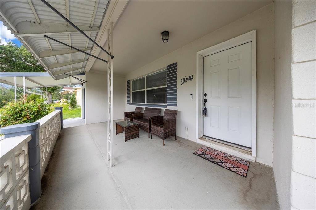 A covered front porch features a white door, wicker seating, and a decorative concrete railing — 30 N LINCOLN AVENUE, BEVERLY HILLS, FL