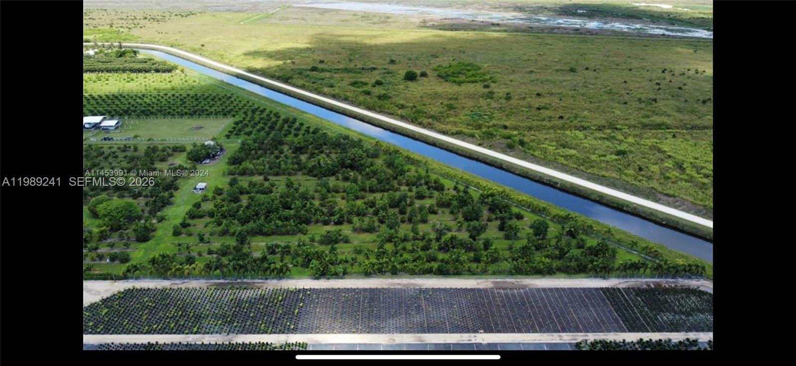 An aerial view shows a canal bordering a tree-filled property and a large nursery area — xxxxx SW 184 st, Miami FL 33187, MIAMI, FL