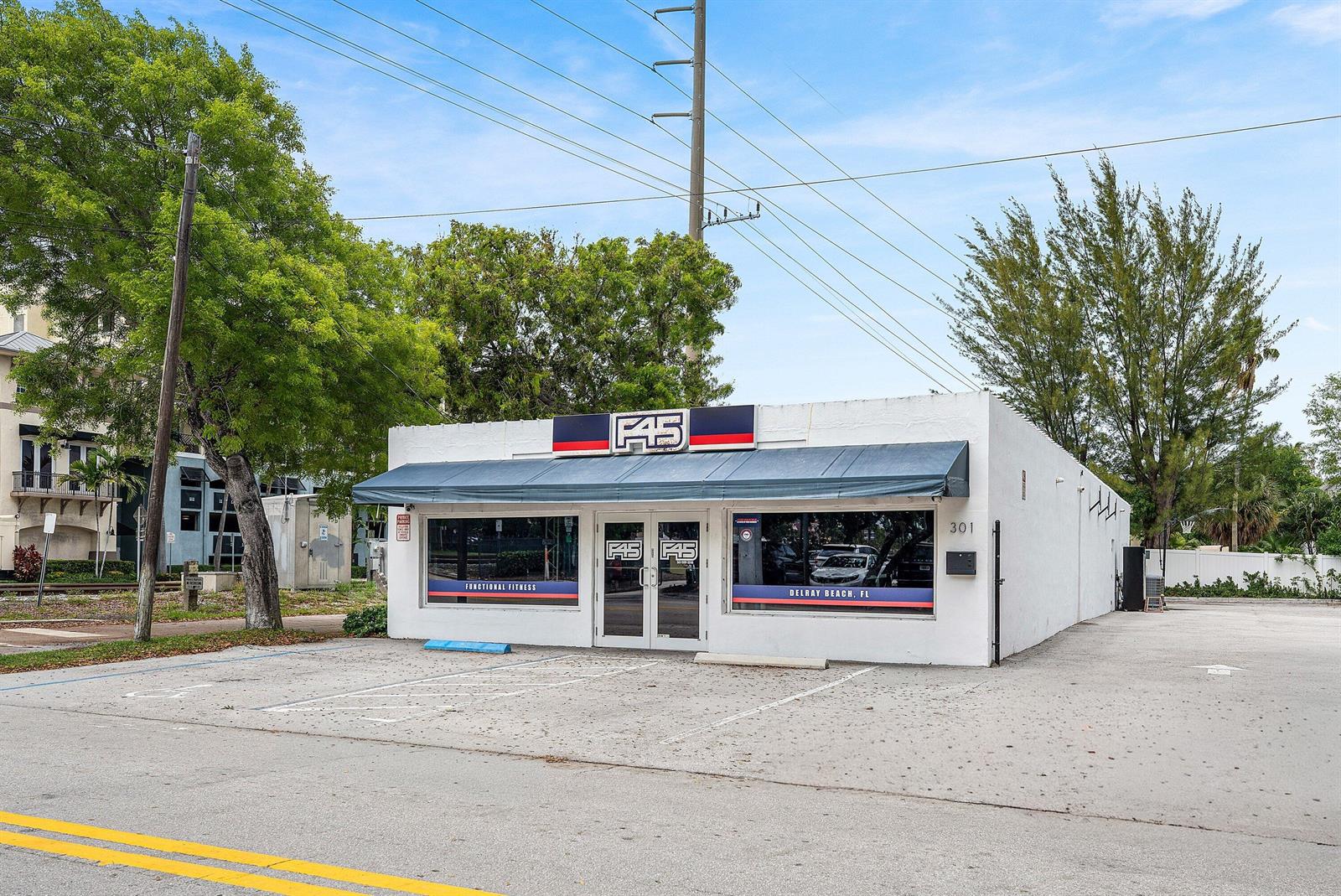 A white, single-story commercial building with an F45 fitness studio sign and a blue awning — 301 NE 1st Street, Delray Beach FL 33483, DELRAY BEACH, FL
