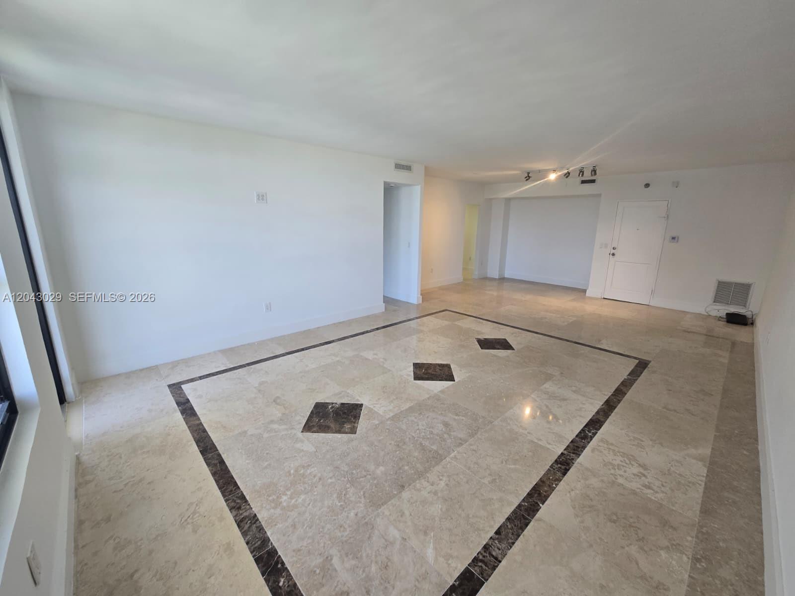 An empty room features white walls, recessed lighting, and beige tile flooring with dark decorative accents — BAL HARBOUR, FL