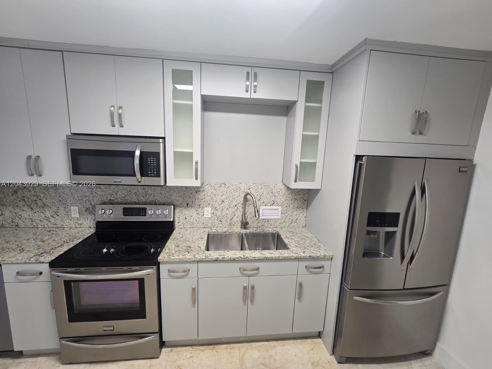 A kitchen features light gray cabinets, granite countertops, and stainless steel appliances — BAL HARBOUR, FL
