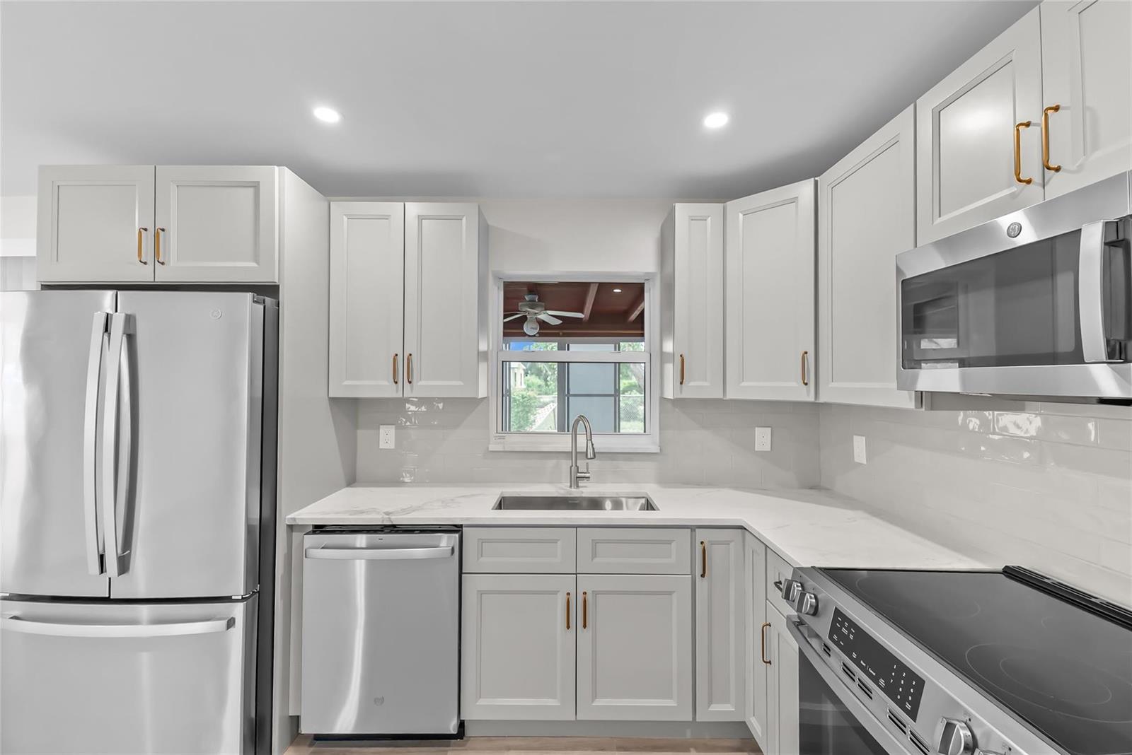 A modern kitchen features light gray cabinets, stainless steel appliances, and white marble-look countertops — 908 Lighthouse Drive, North Palm Beach FL 33408, NORTH PALM BEACH, FL
