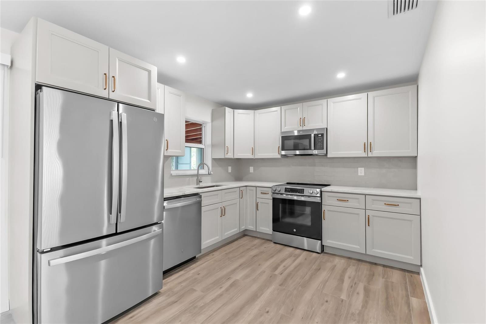 A kitchen with light gray cabinets, stainless steel appliances, and light wood-look flooring — 908 Lighthouse Drive, North Palm Beach FL 33408, NORTH PALM BEACH, FL