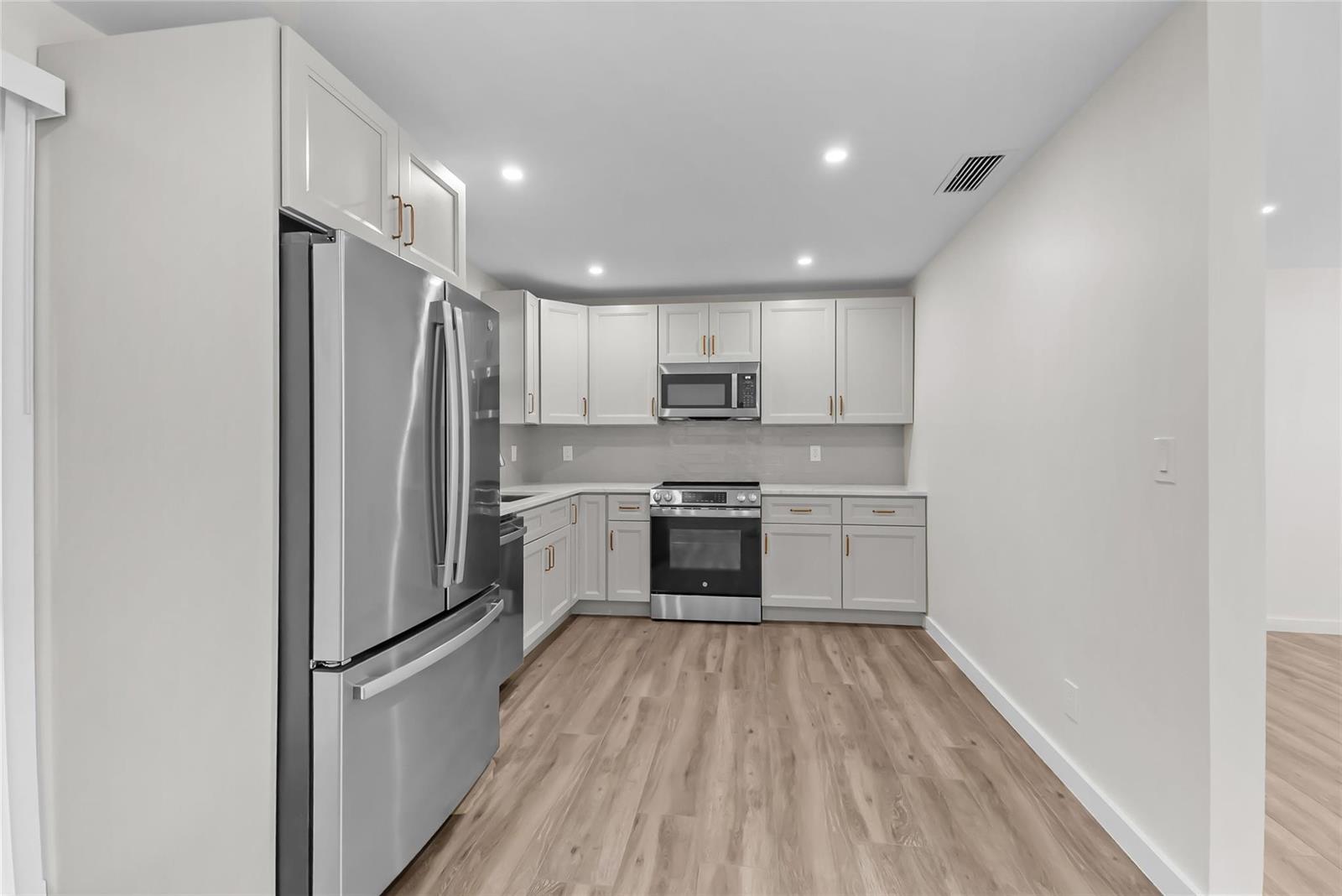 A kitchen features light gray cabinets, stainless steel appliances, and light wood-look flooring — 908 Lighthouse Drive, North Palm Beach FL 33408, NORTH PALM BEACH, FL