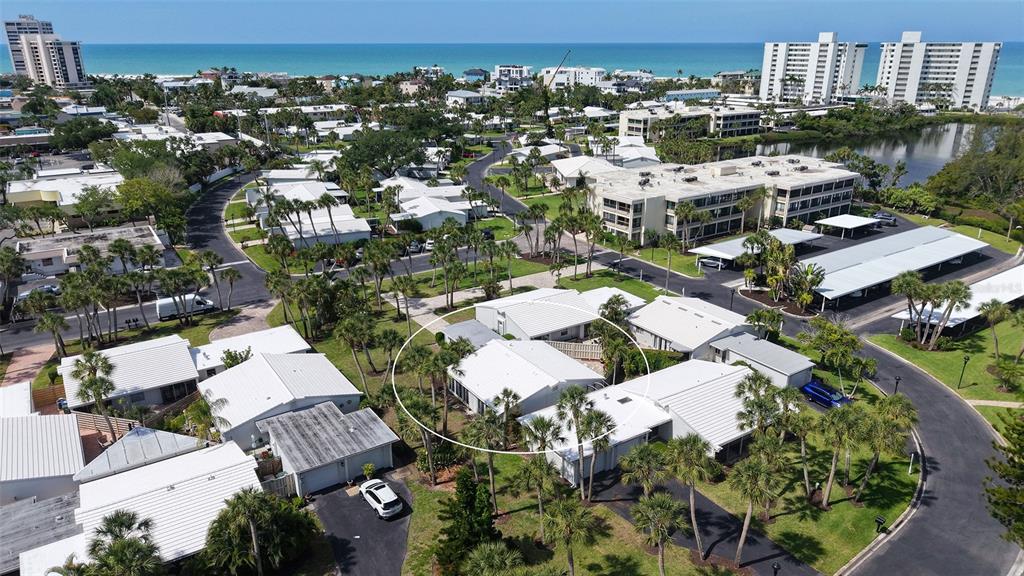 An aerial view shows a white-roofed residential building surrounded by palm trees and paved roads — 206 HOURGLASS WAY UNIT V10, SARASOTA, FL