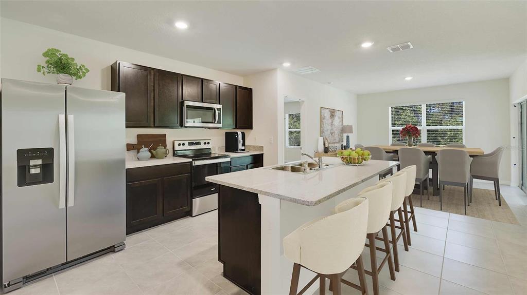 A kitchen features dark wood cabinets, stainless steel appliances, a white island, and dining area — 8609 TIDEWATER TRAIL AVENUE, TEMPLE TERRACE, FL
