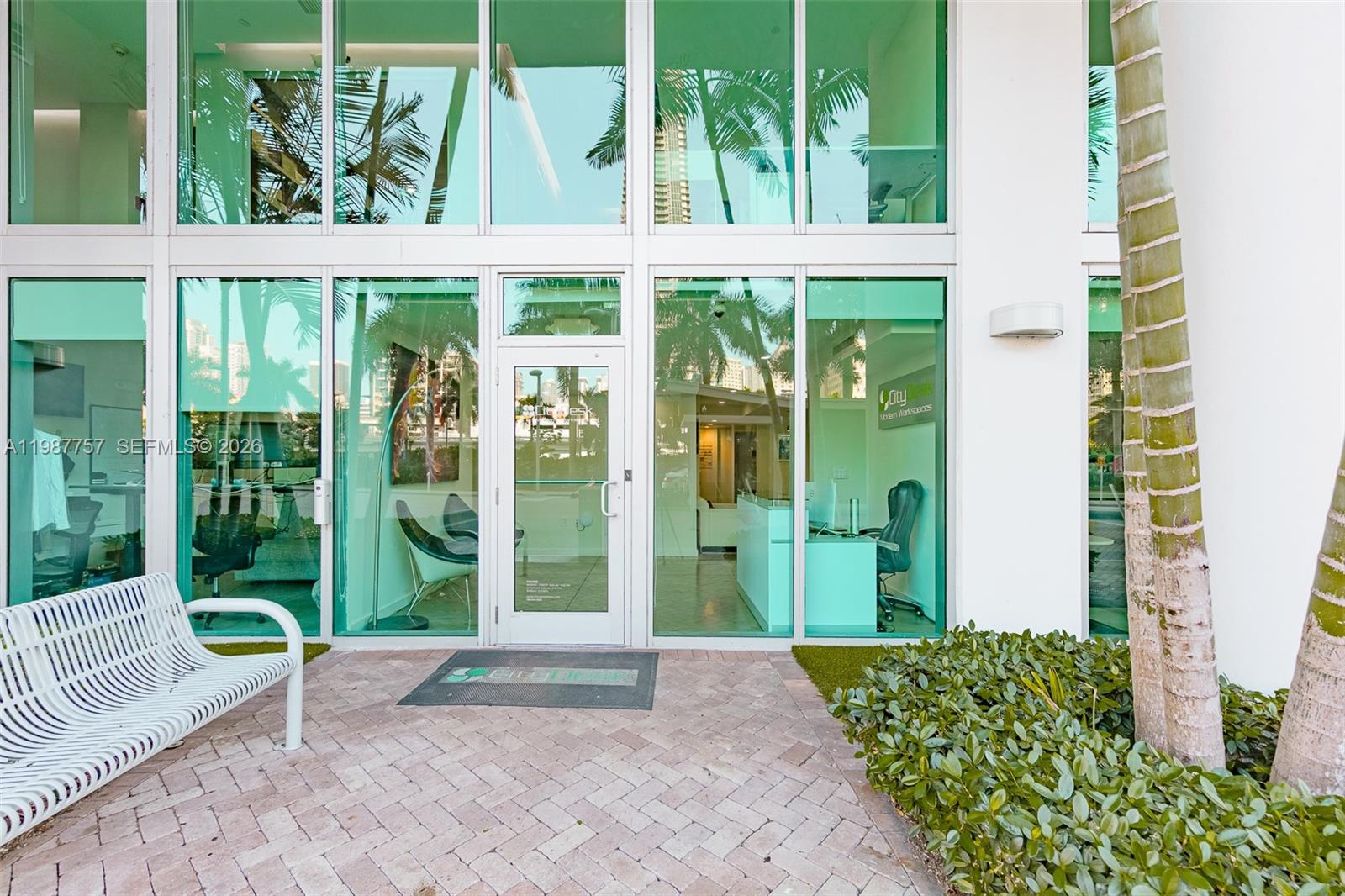 The exterior of a modern office building features glass walls, a white bench, and landscaping — 350 S Miami Avenue, Miami FL 33130, MIAMI, FL