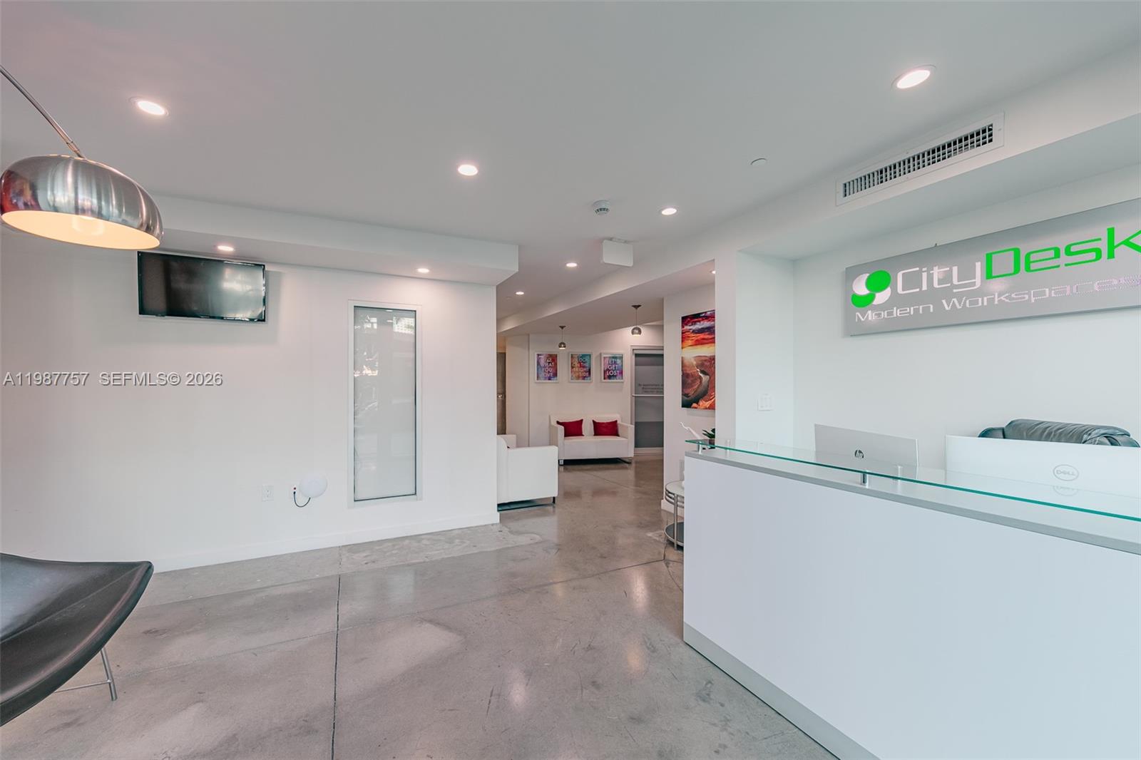 A modern office reception area features a white desk, concrete floors, and recessed lighting — 350 S Miami Avenue, Miami FL 33130, MIAMI, FL