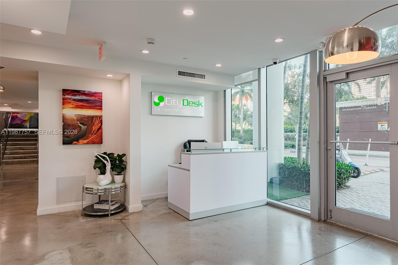 A modern office reception area features a white desk, glass walls, and a landscape painting — 350 S Miami Avenue, Miami FL 33130, MIAMI, FL