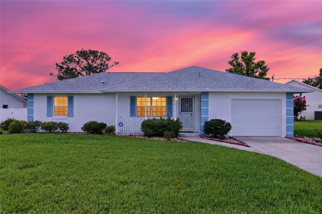 A single-story white house with blue shutters and a garage under a vibrant sunset sky — 48 BANYAN TRACK, OCALA, FL