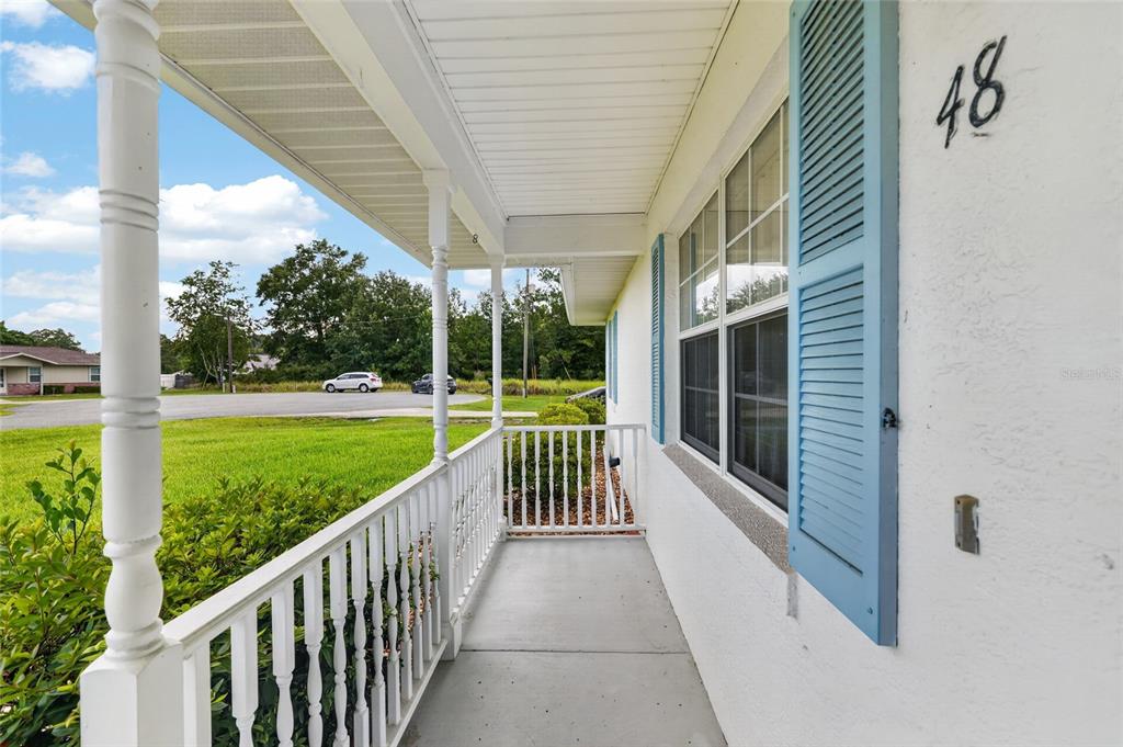 A covered front porch with white railings and blue shutters on a white house — 48 BANYAN TRACK, OCALA, FL