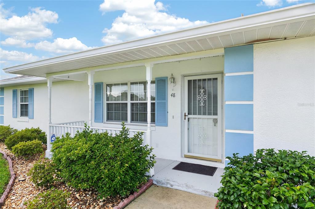 A white house exterior features a covered porch, blue shutters, and a storm door — 48 BANYAN TRACK, OCALA, FL