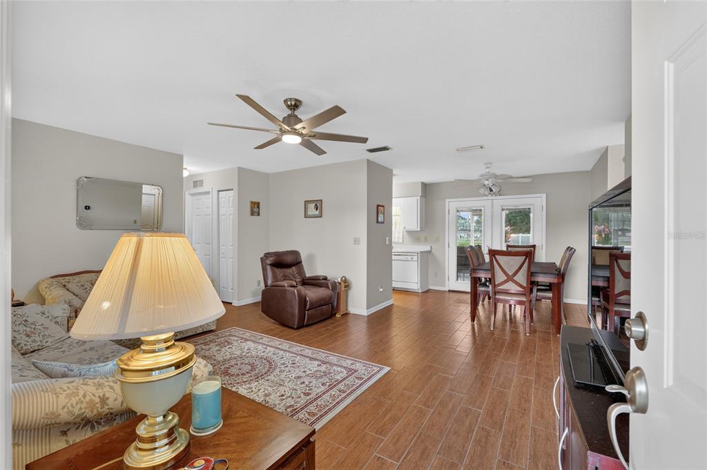 A living and dining area features wood-look tile flooring, a ceiling fan, and neutral walls — 48 BANYAN TRACK, OCALA, FL