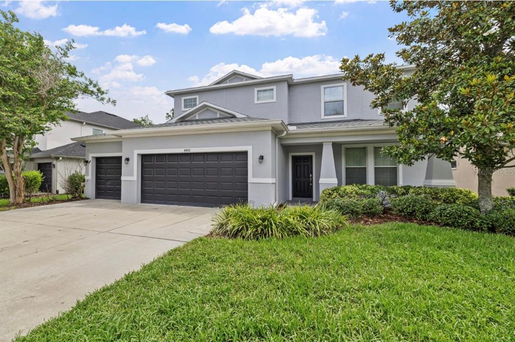 A two-story house with a gray exterior, a three-car garage, and a front lawn — 4400 WILDSTAR CIRCLE, WESLEY CHAPEL, FL