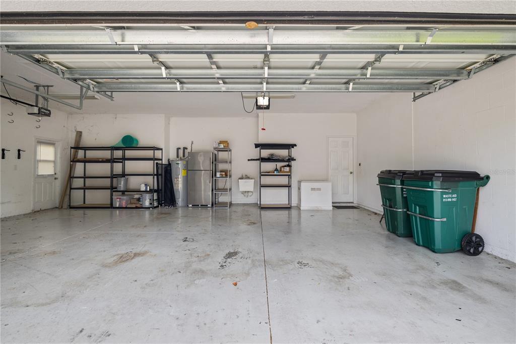 A spacious two-car garage with white walls, concrete flooring, metal shelving, and two green bins — 4400 WILDSTAR CIRCLE, WESLEY CHAPEL, FL