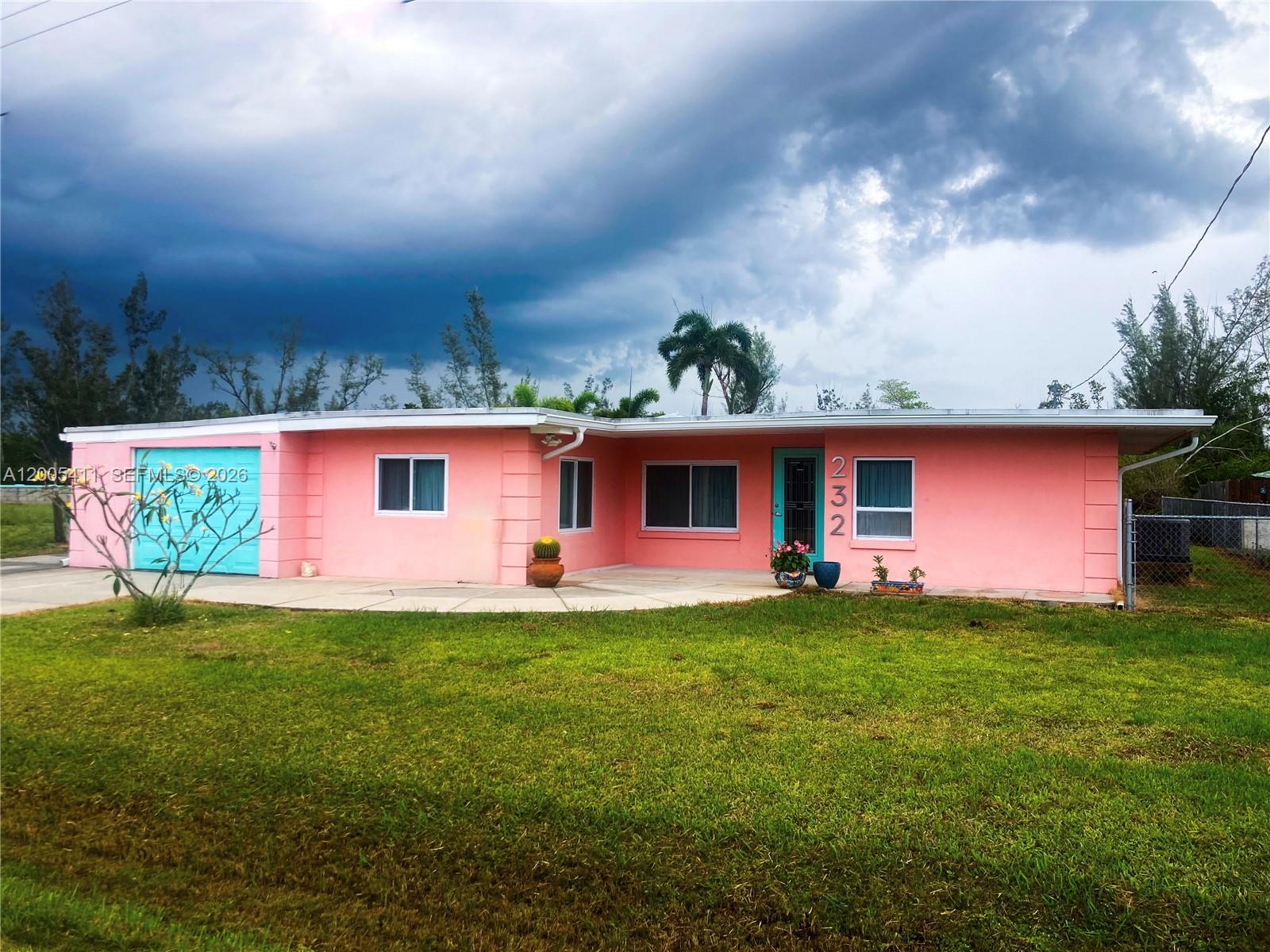 A single-story pink house with a turquoise garage door and front door under a cloudy sky — 232 DARST AVE, Punta Gorda FL 33950, PUNTA GORDA, FL