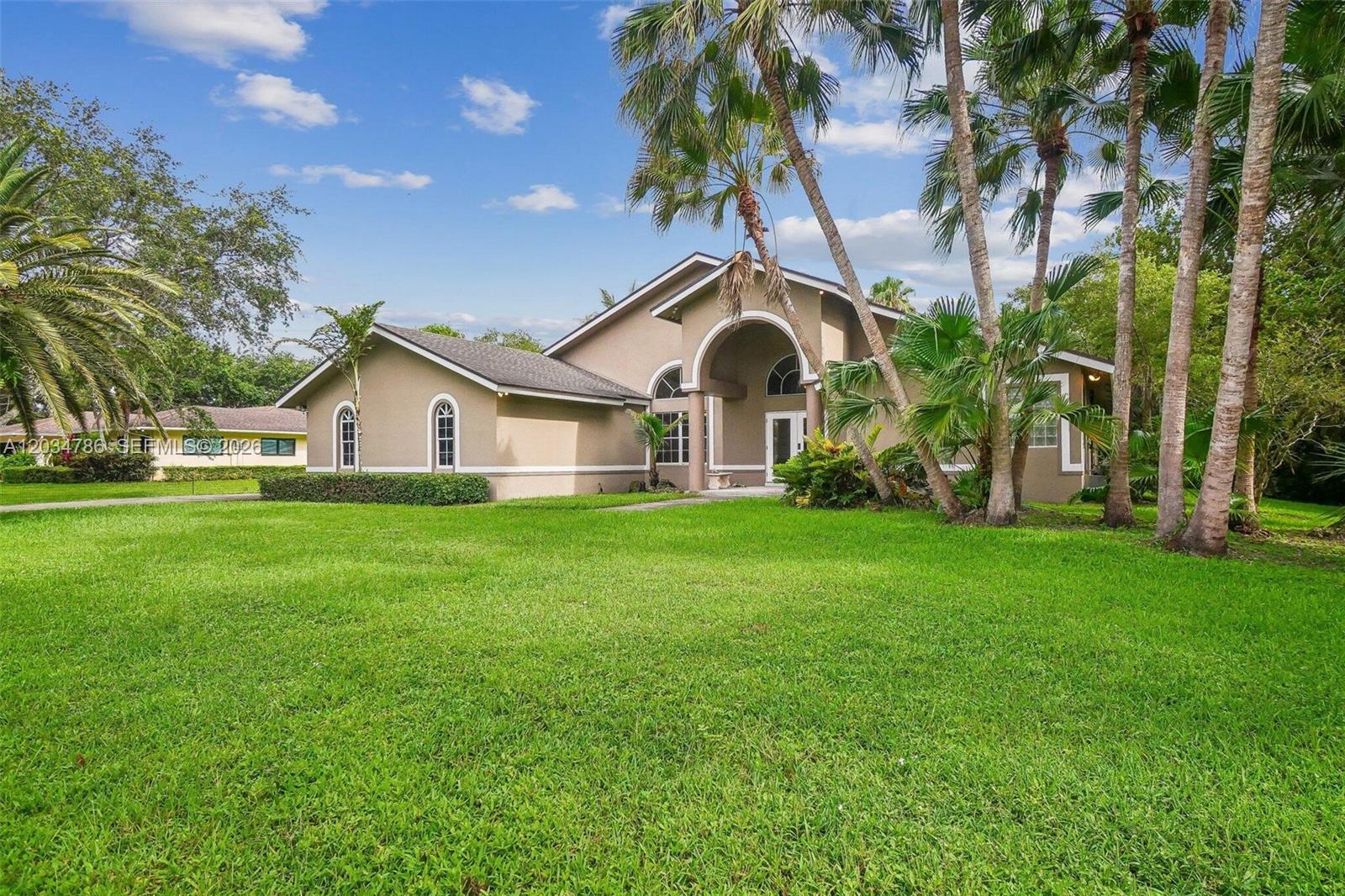 A tan, single-story house with an arched entryway sits on a large, grassy lawn — 14591 SW 23rd St, Davie FL 33325, DAVIE, FL