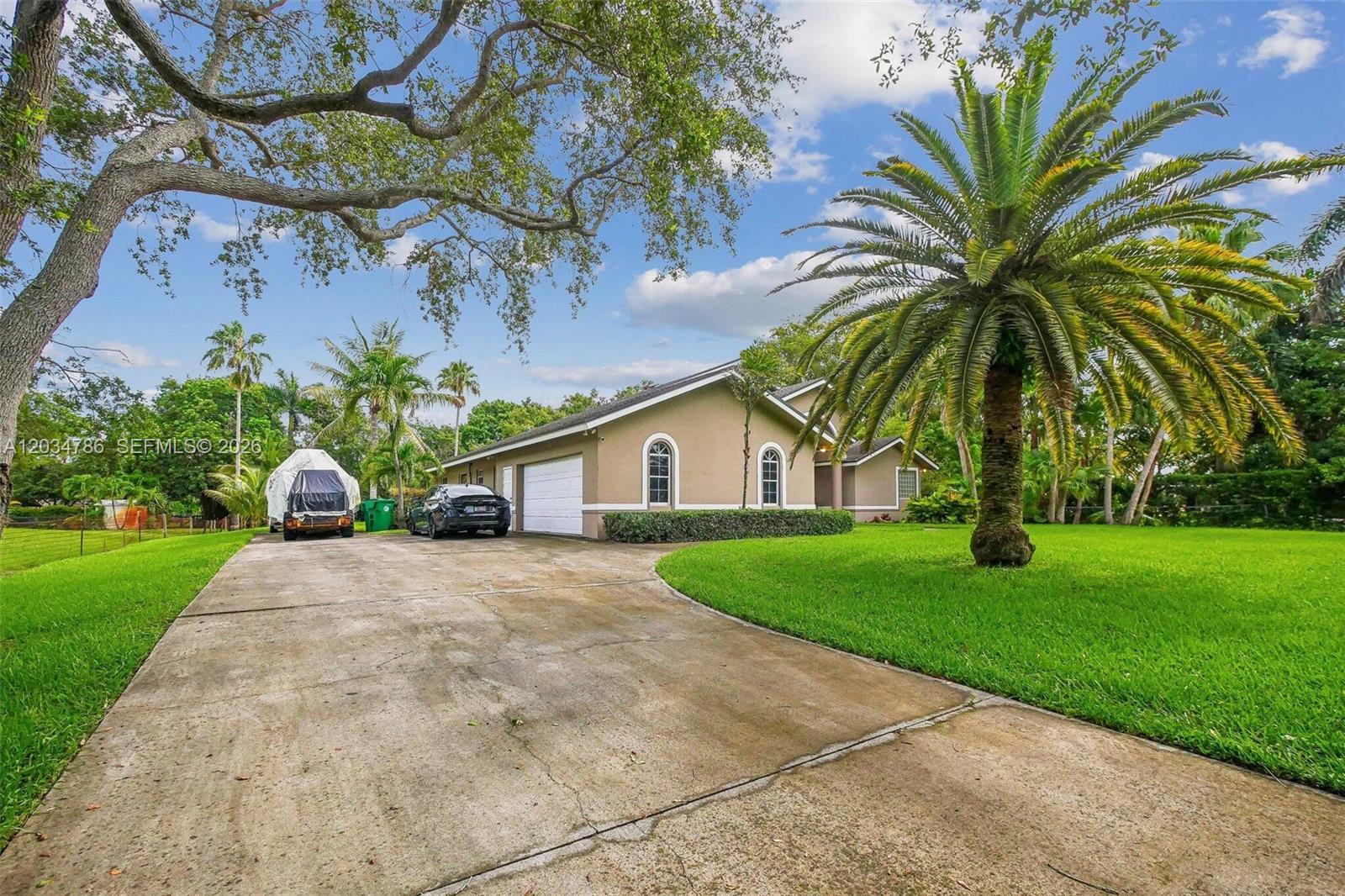 A tan house with a concrete driveway, a palm tree, and a large oak tree — 14591 SW 23rd St, Davie FL 33325, DAVIE, FL