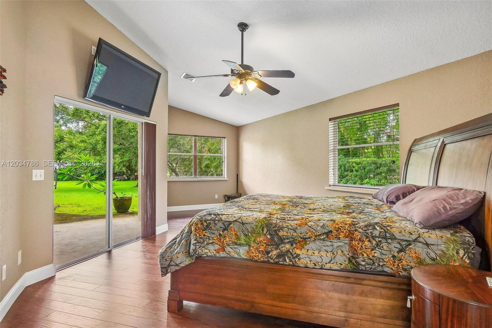 A bedroom features a wooden bed, ceiling fan, sliding glass doors, and views of greenery — 14591 SW 23rd St, Davie FL 33325, DAVIE, FL