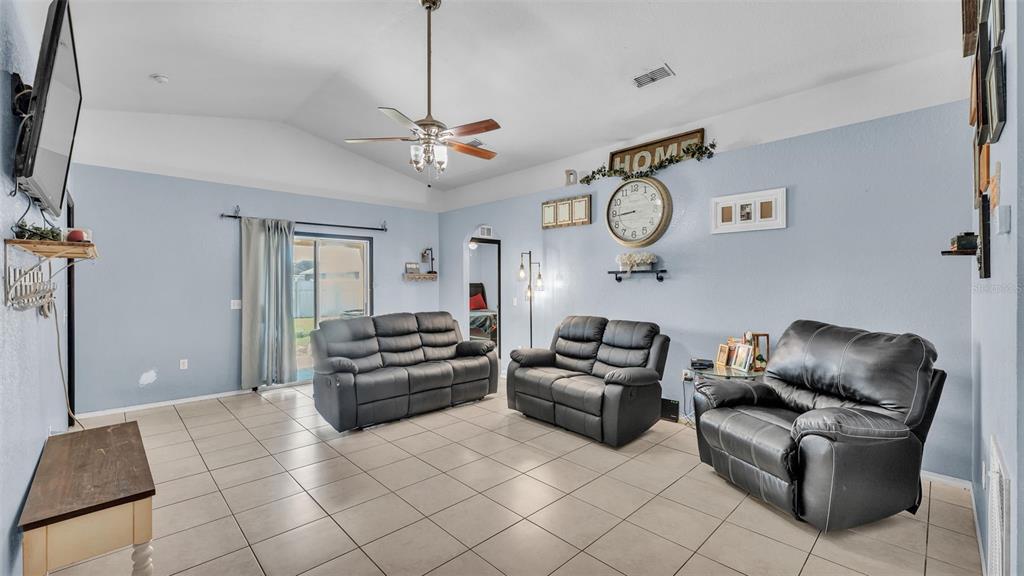 A living room features light blue walls, tile flooring, a ceiling fan, and three leather sofas — 834 AUBURN PRESERVE BOULEVARD, AUBURNDALE, FL