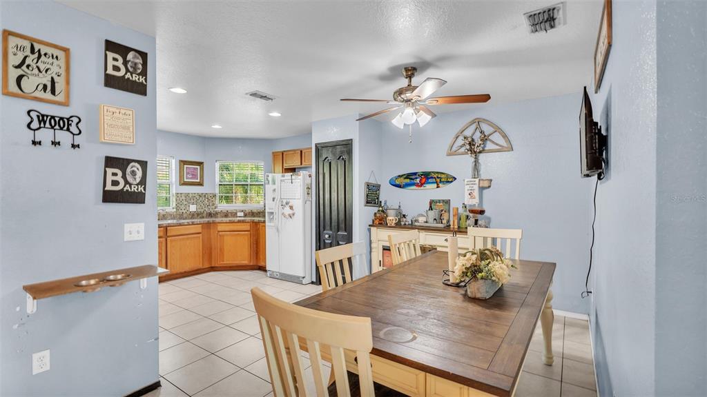 A dining area with a wooden table and chairs opens into a kitchen with cabinets — 834 AUBURN PRESERVE BOULEVARD, AUBURNDALE, FL