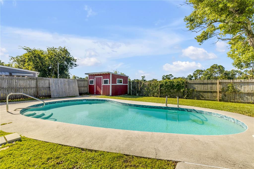 A backyard features a kidney-shaped swimming pool, a red storage shed, and a wooden fence — 709 TARRY TOWN TRAIL, PORT ORANGE, FL