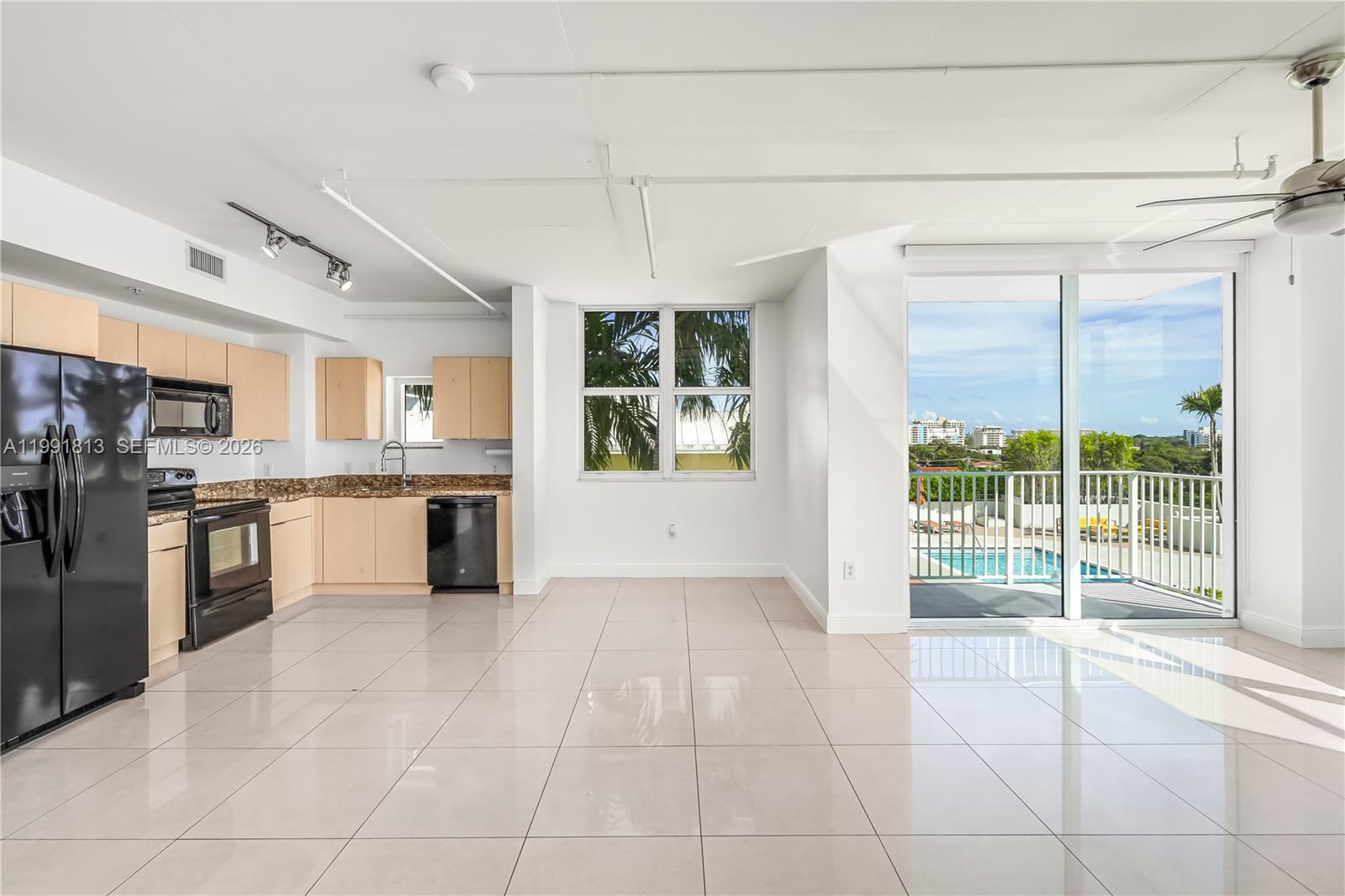 A kitchen and living area with light wood cabinets, black appliances, and a balcony view — 3180 SW 22nd St # 601, Miami FL 33145, MIAMI, FL
