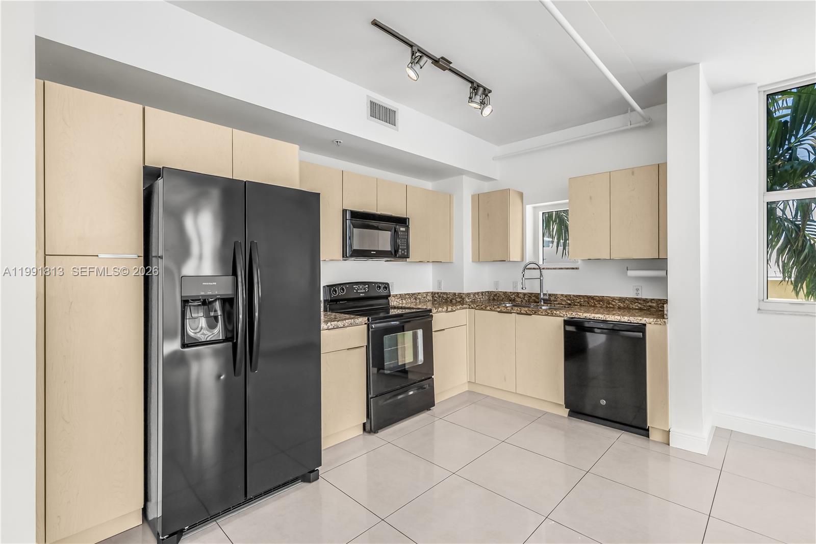 This kitchen features light wood cabinets, black appliances, granite countertops, and large floor tiles — 3180 SW 22nd St # 601, Miami FL 33145, MIAMI, FL